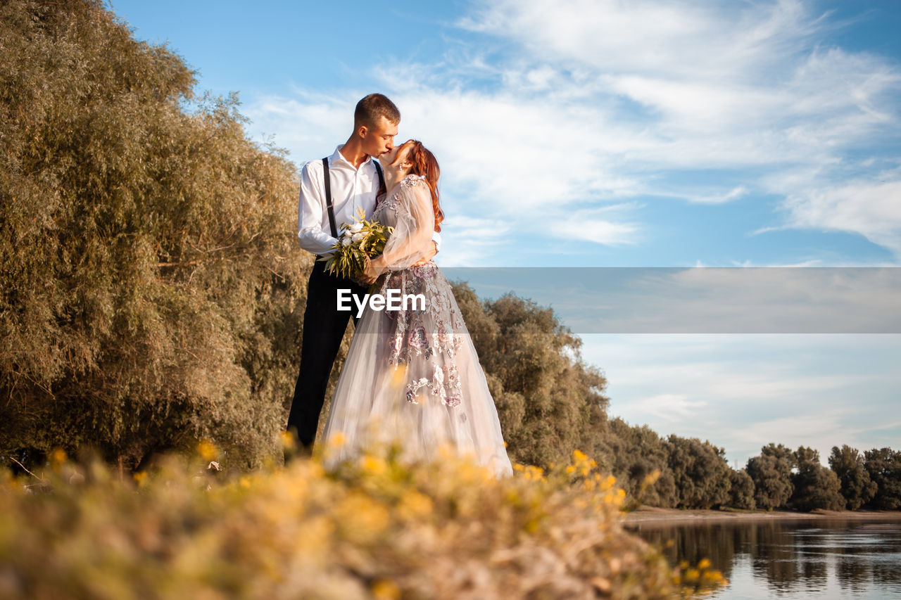 A young wedding couple in love on the edge of a cliff against the backdrop of the river and the sky.