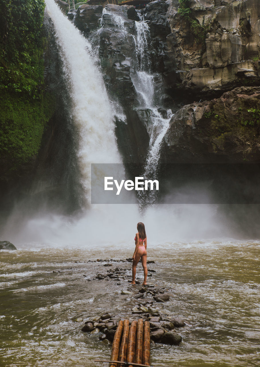 Young woman standing against waterfall