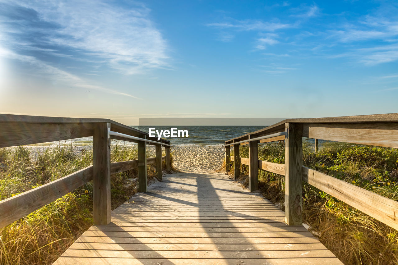 Footbridge at beach against sky in sunny day