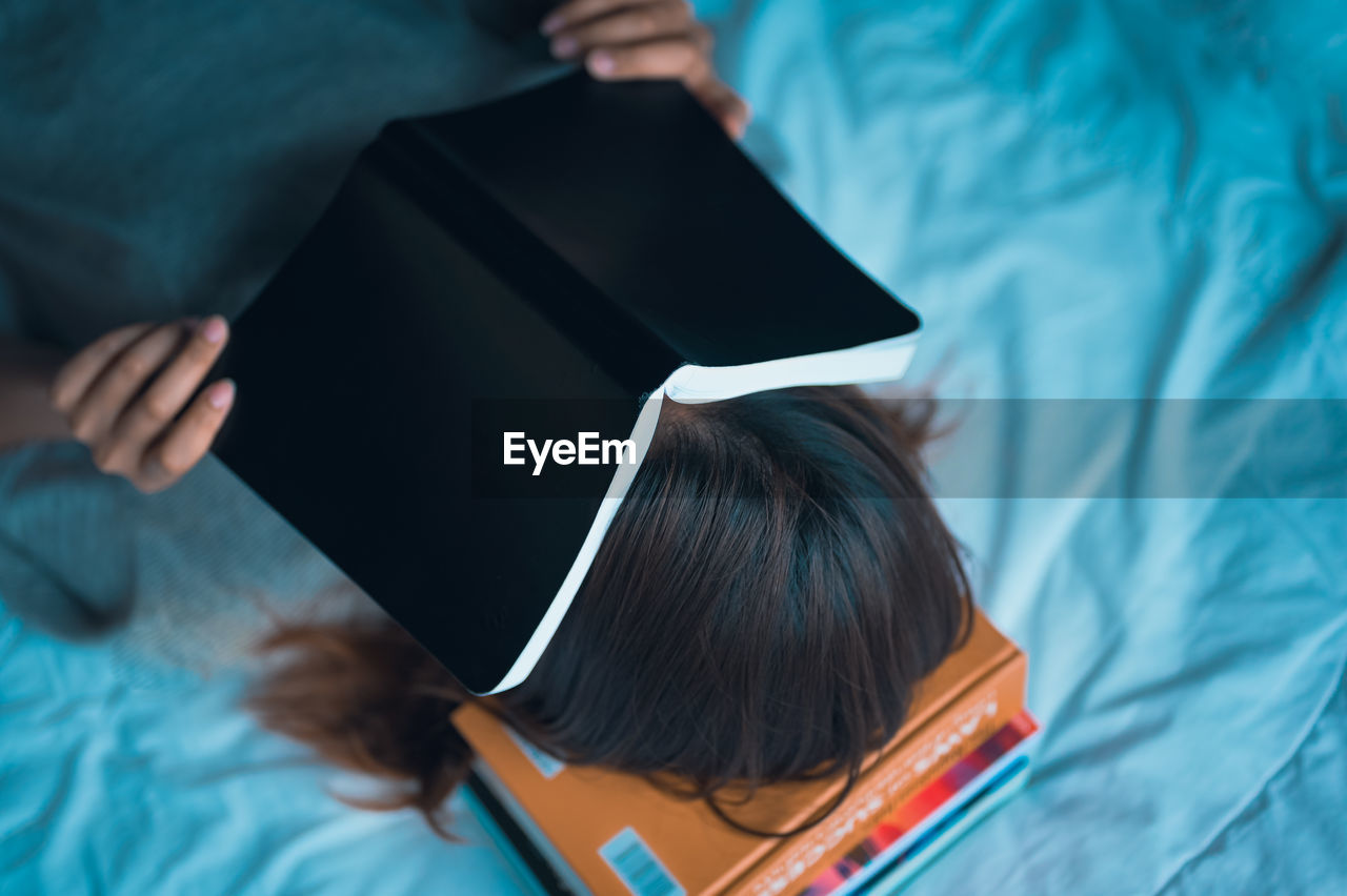  young women lie down on pile of book and cover her face by the book education and growth concept