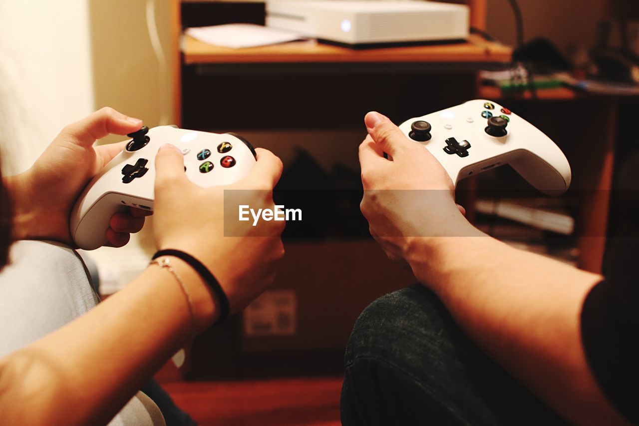 Cropped hands of friends playing video game at home