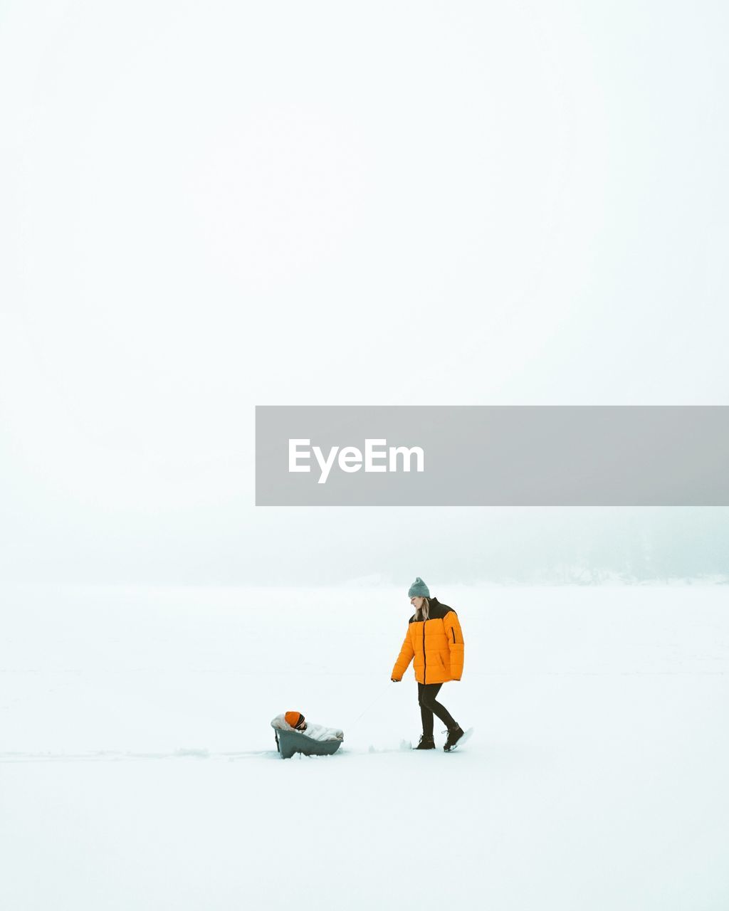 MAN WITH UMBRELLA WALKING ON SNOW COVERED LANDSCAPE AGAINST CLEAR SKY