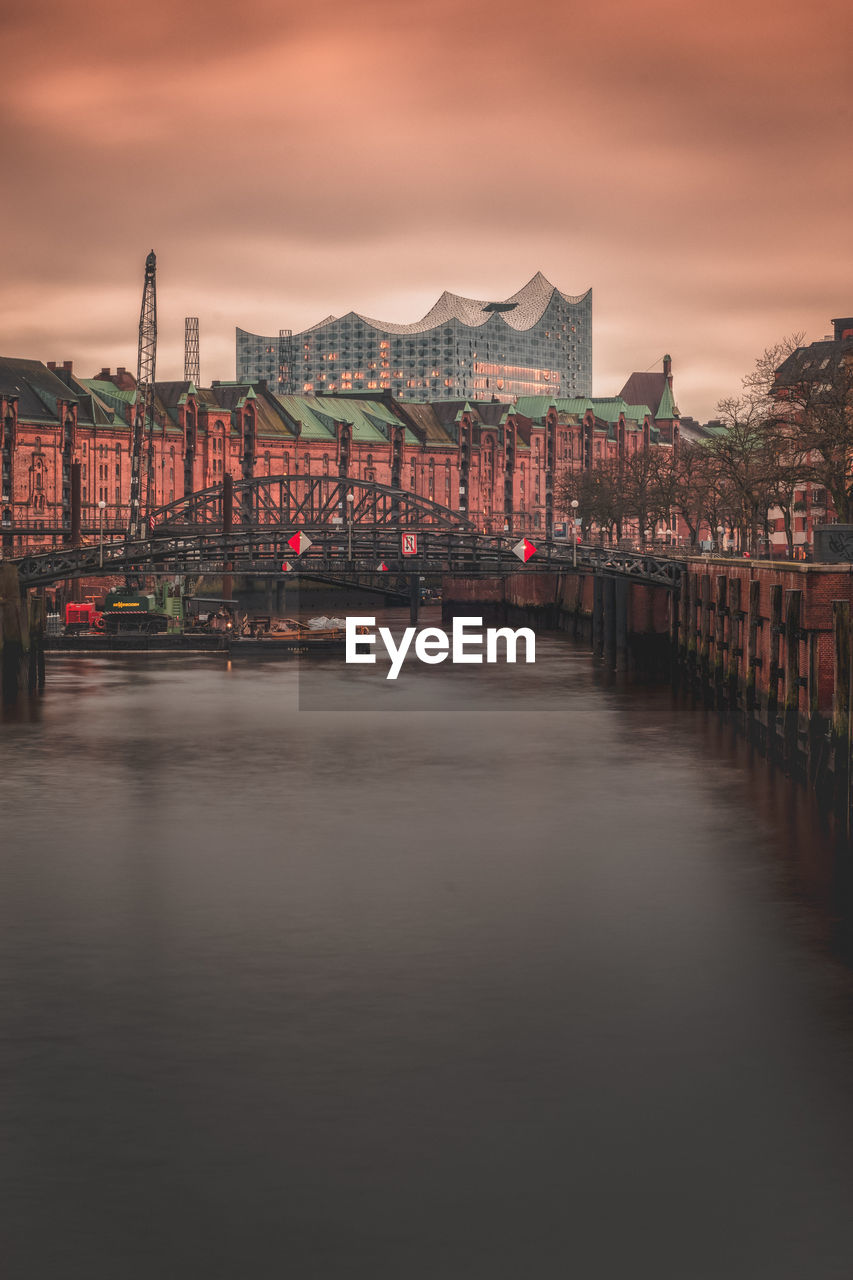 Bridge over river amidst buildings in city at sunset