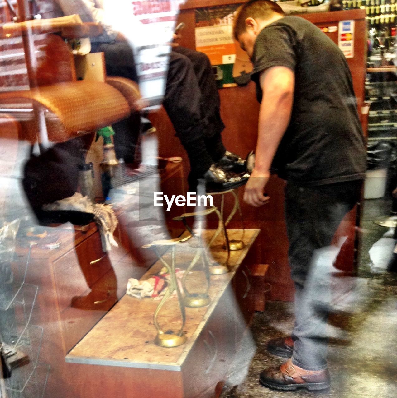 View of man shinning shoes through glass