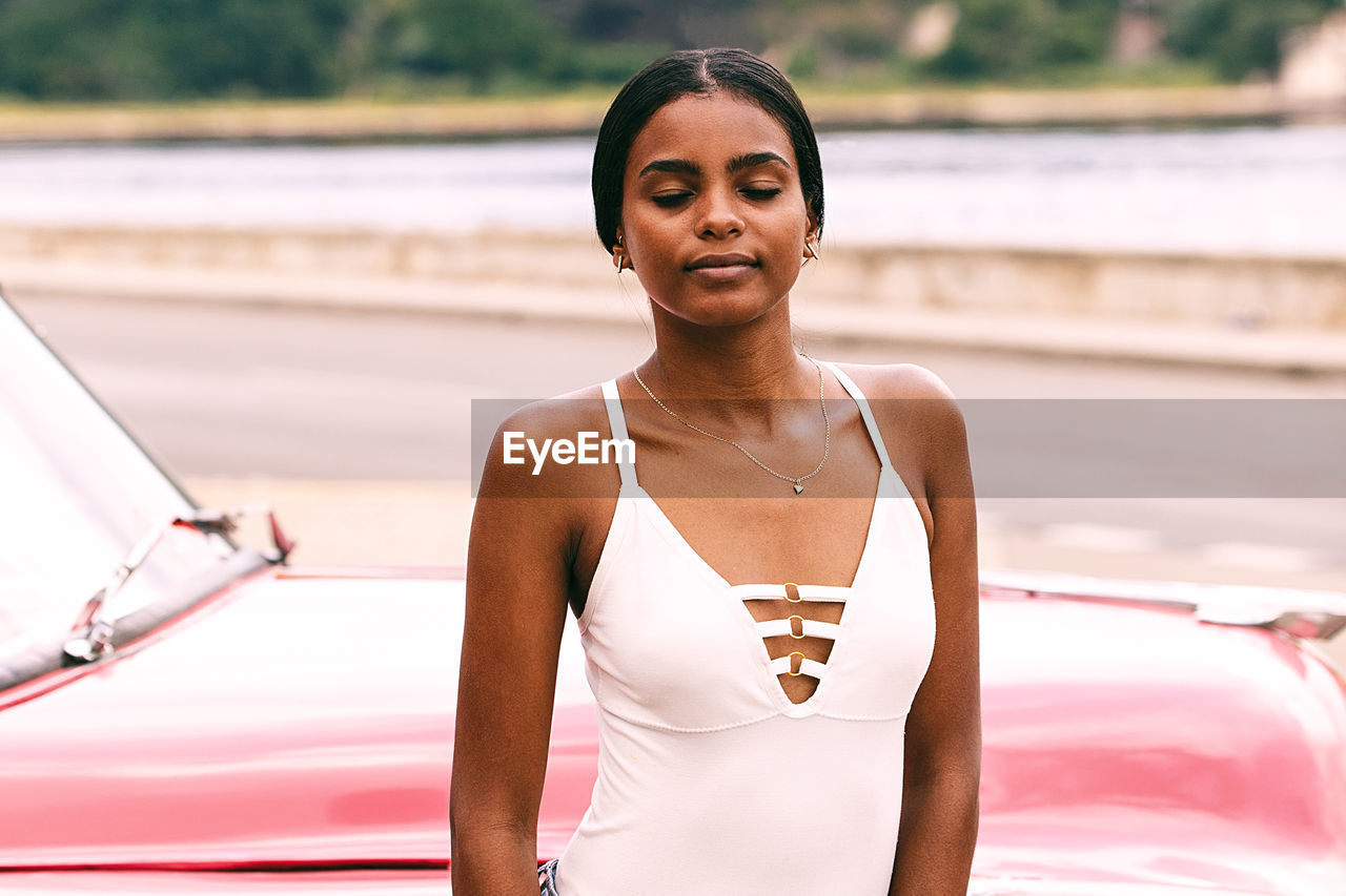 Woman in dress with eyes closed standing against car