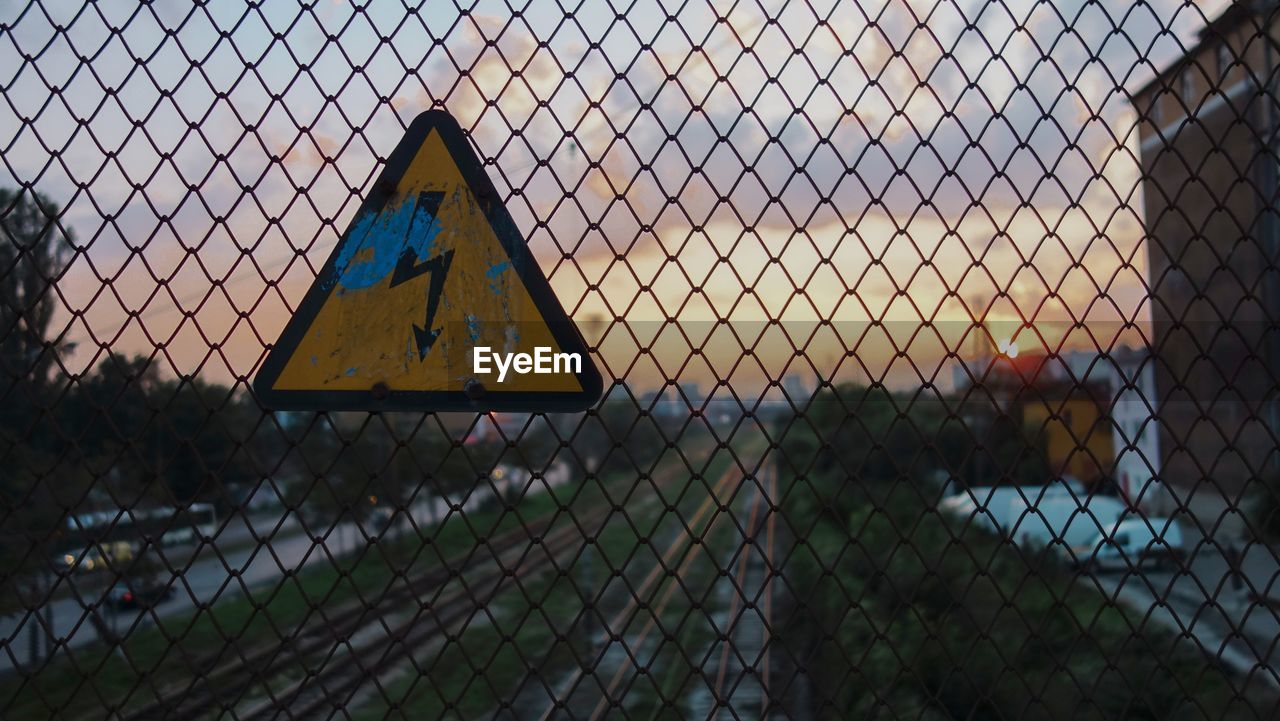 High voltage sign on chainlink fence at sunset