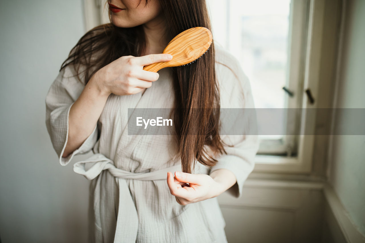 MIDSECTION OF WOMAN HOLDING ICE CREAM STANDING IN KITCHEN