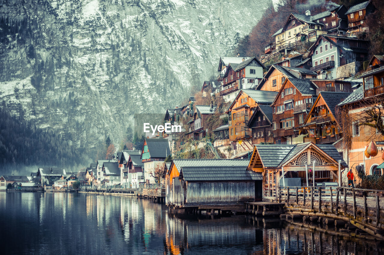 Lake by houses against snow covered mountain
