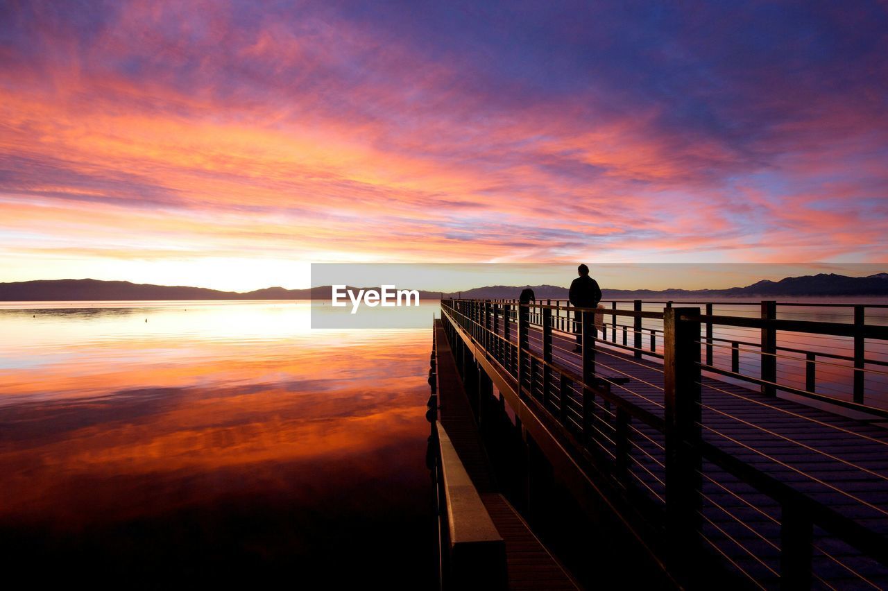 SILHOUETTE MAN STANDING ON RAILING AGAINST SEA