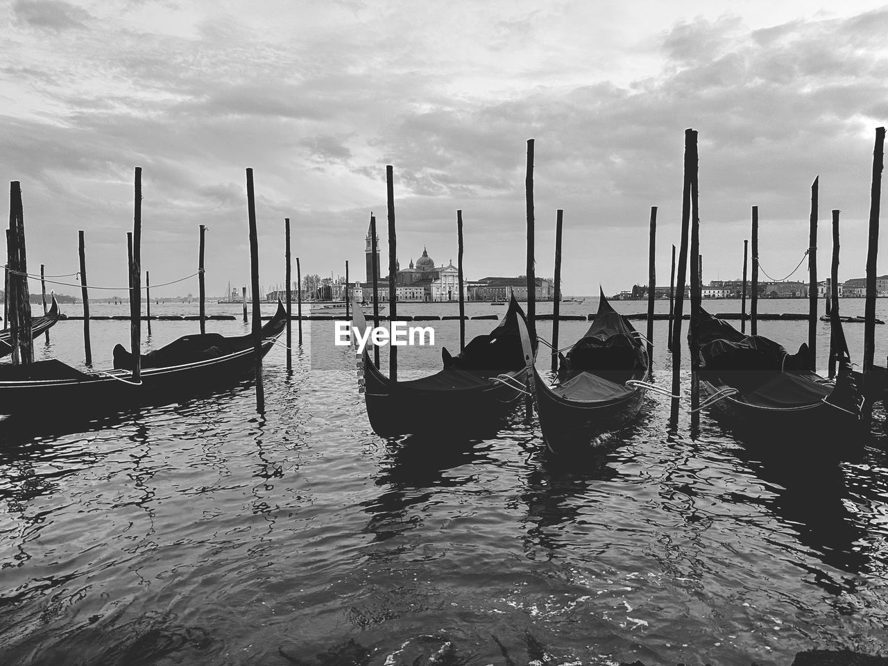 nautical vessel, water, gondola, transportation, mode of transportation, black and white, boat, sea, nature, sky, travel destinations, vehicle, travel, monochrome, monochrome photography, cloud, wooden post, moored, architecture, canal, lagoon, wood, post, tourism, no people, outdoors, watercraft, scenics - nature, boating, pier, beauty in nature, pole, in a row, tranquility, idyllic