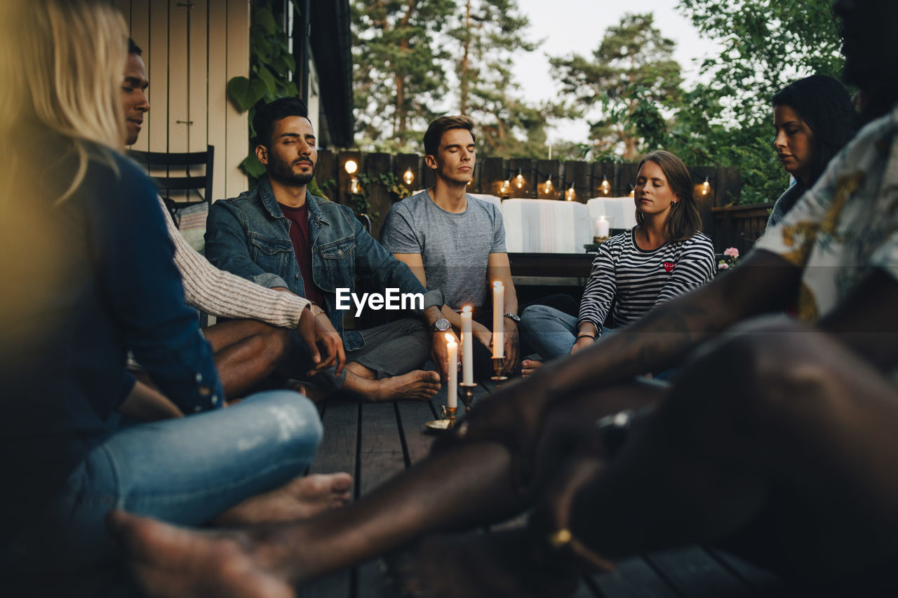 Male and female friends sitting with eyes closed in balcony during group session