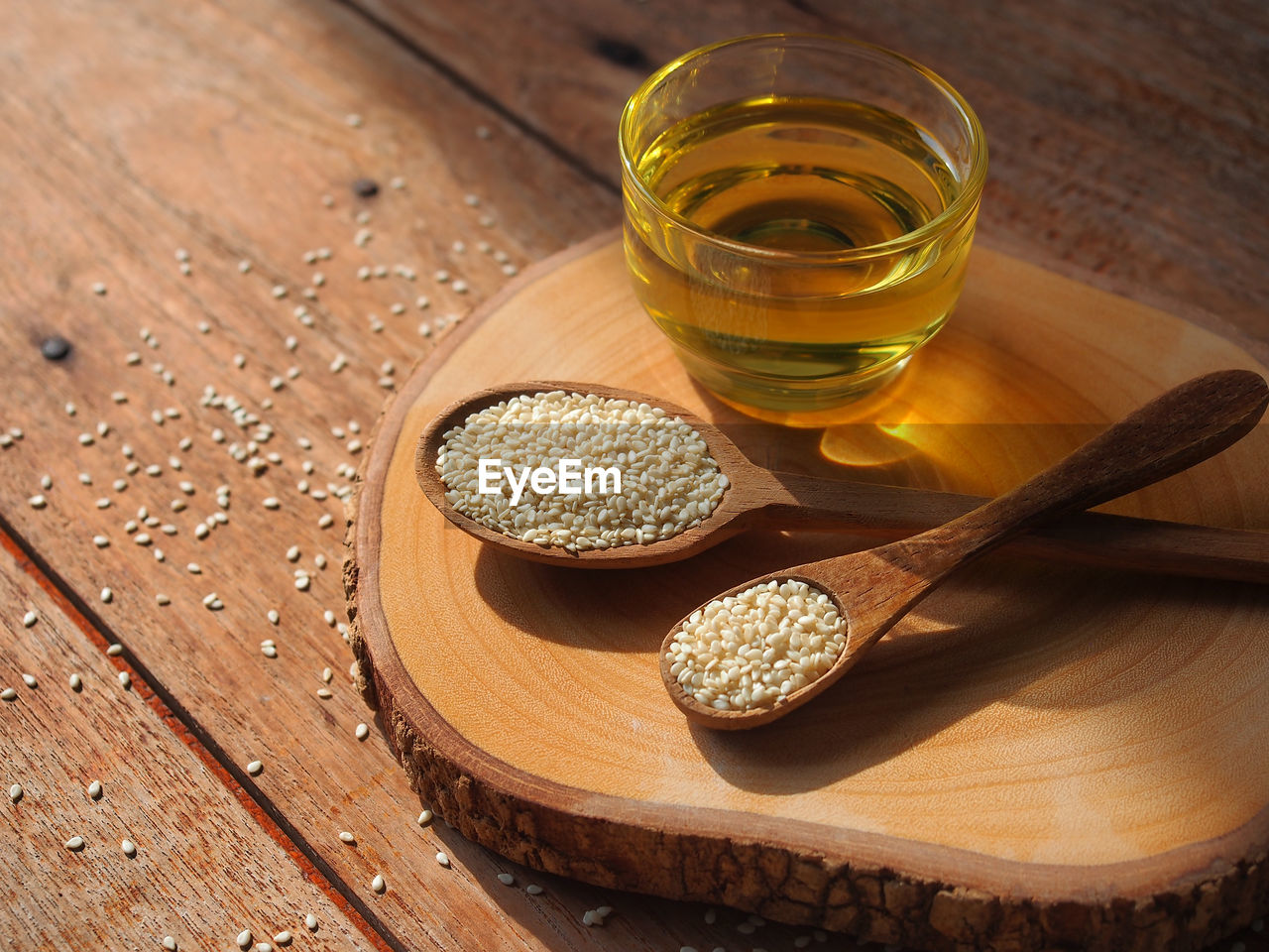 White sesame seeds in wooden spoon and a glass of sesame oil for healthy food concept.