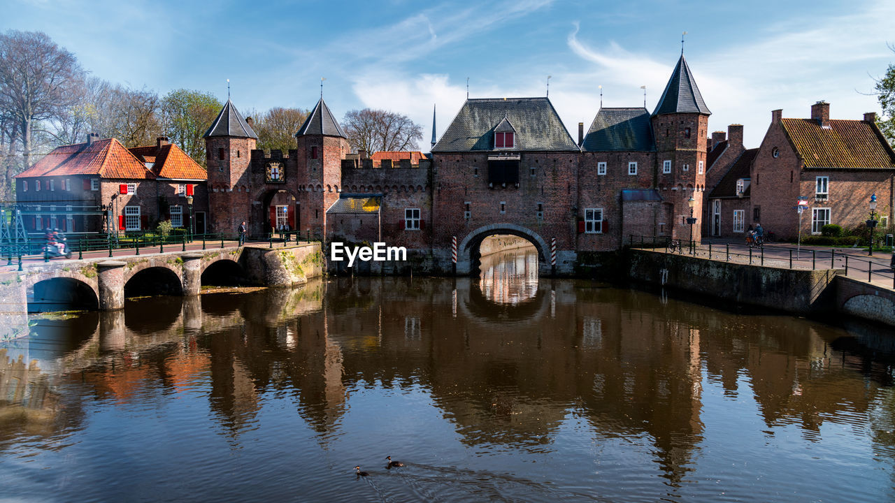 REFLECTION OF BRIDGE AND BUILDINGS ON RIVER AGAINST SKY