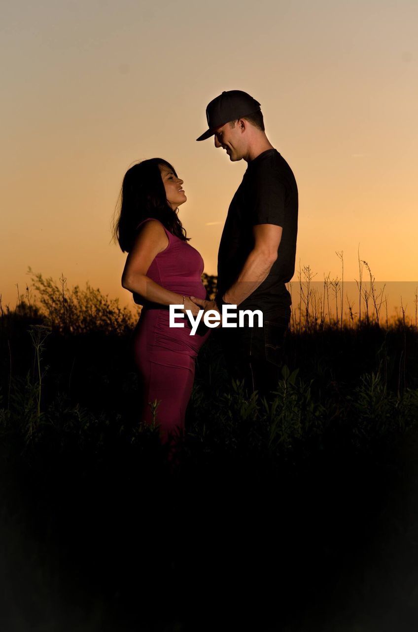 SIDE VIEW OF YOUNG COUPLE STANDING AGAINST SKY