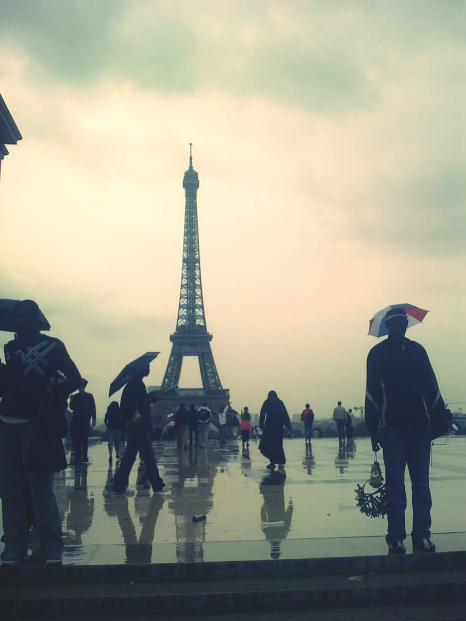 People by eiffel tower against sky on rainy day