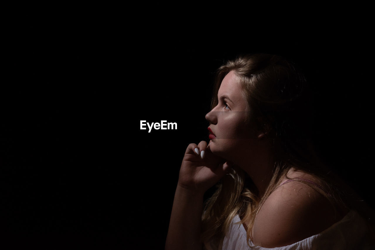 Side view of thoughtful woman looking away against black background