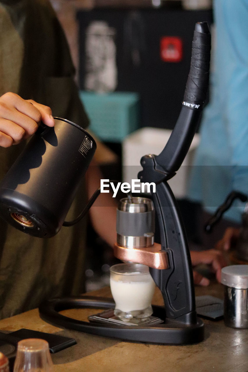 espresso machine, coffeemaker, food and drink, drink, indoors, coffee, home appliance, adult, occupation, one person, refreshment, cafe, holding, business, drip coffee maker, pouring, working, barista, focus on foreground, coffee shop, hand, cup, mug, coffee cup, close-up