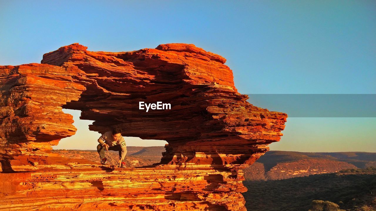 Man crouching in rock formation at desert during sunset