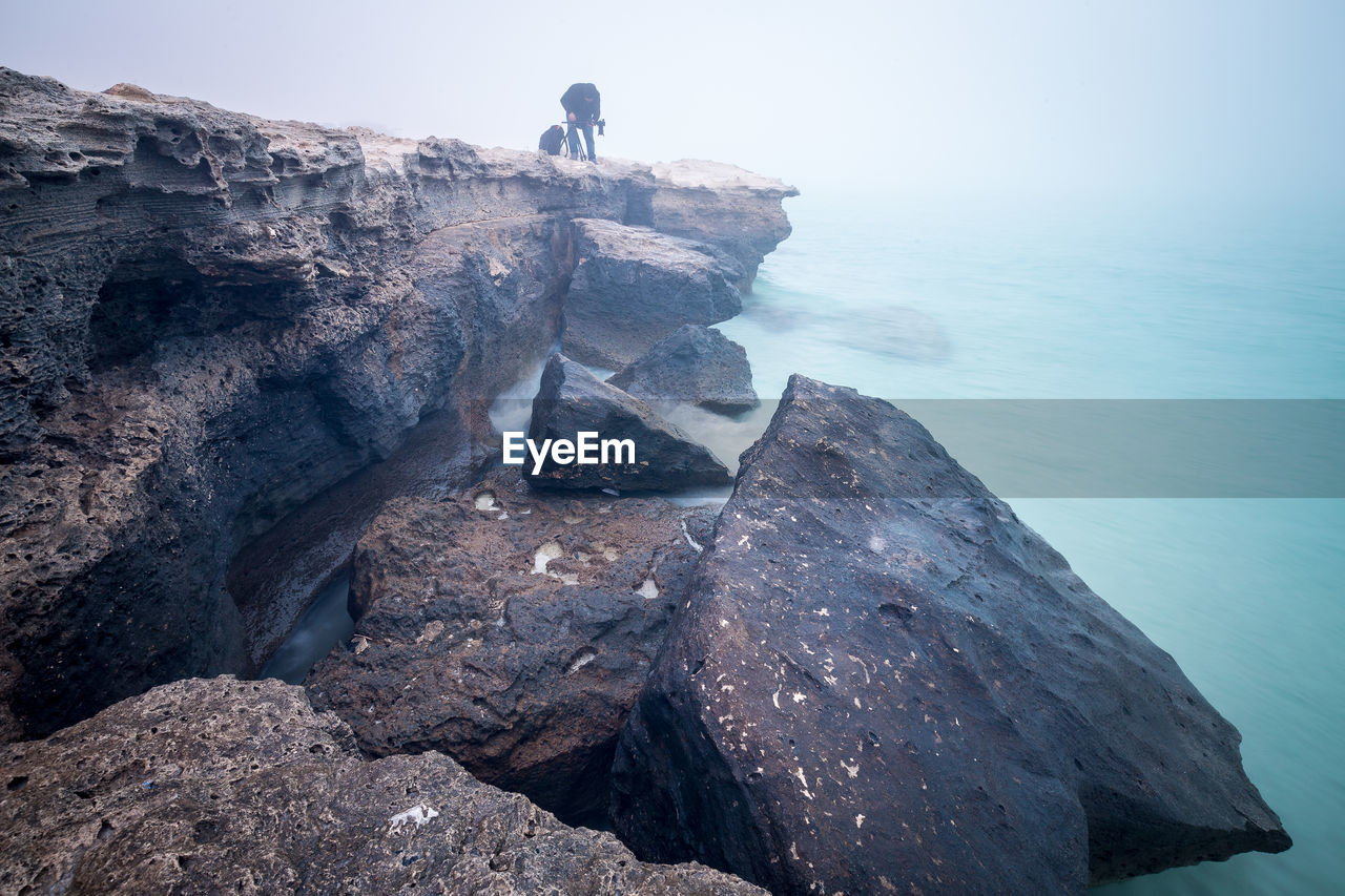 Man standing on cliff by sea against sky