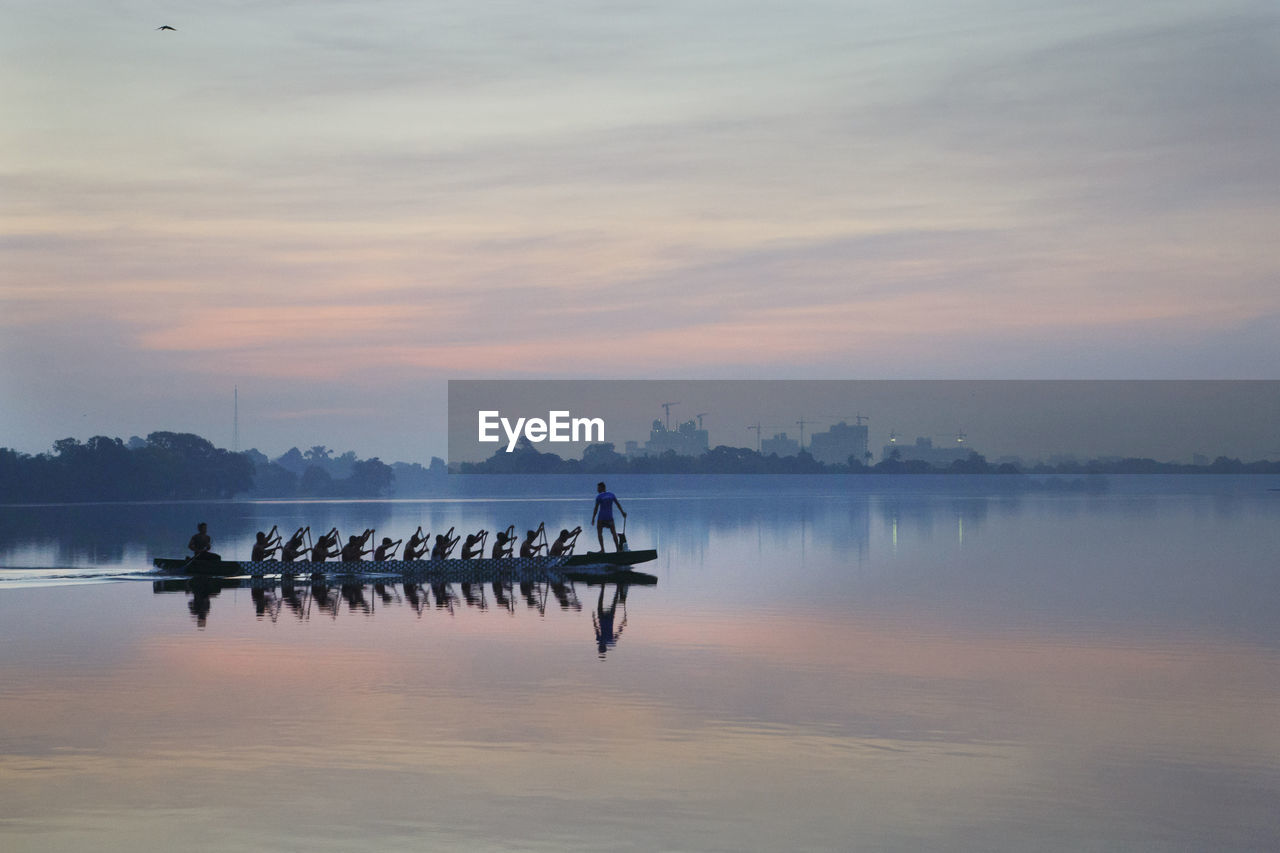 People rowing on lake against during sunrise