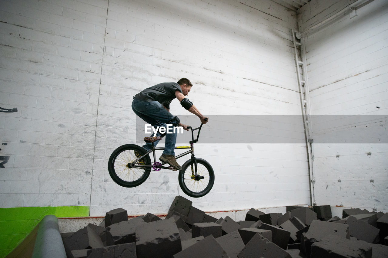 SIDE VIEW OF YOUNG MAN JUMPING ON BICYCLE