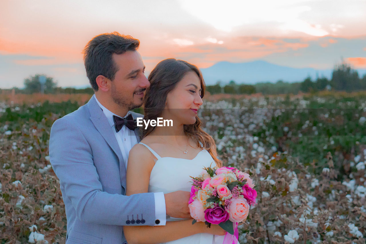 Smiling bride and groom with bouquet romancing on field