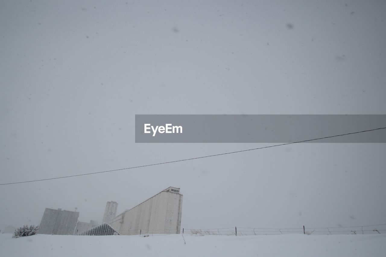 Industry against clear sky during snowfall