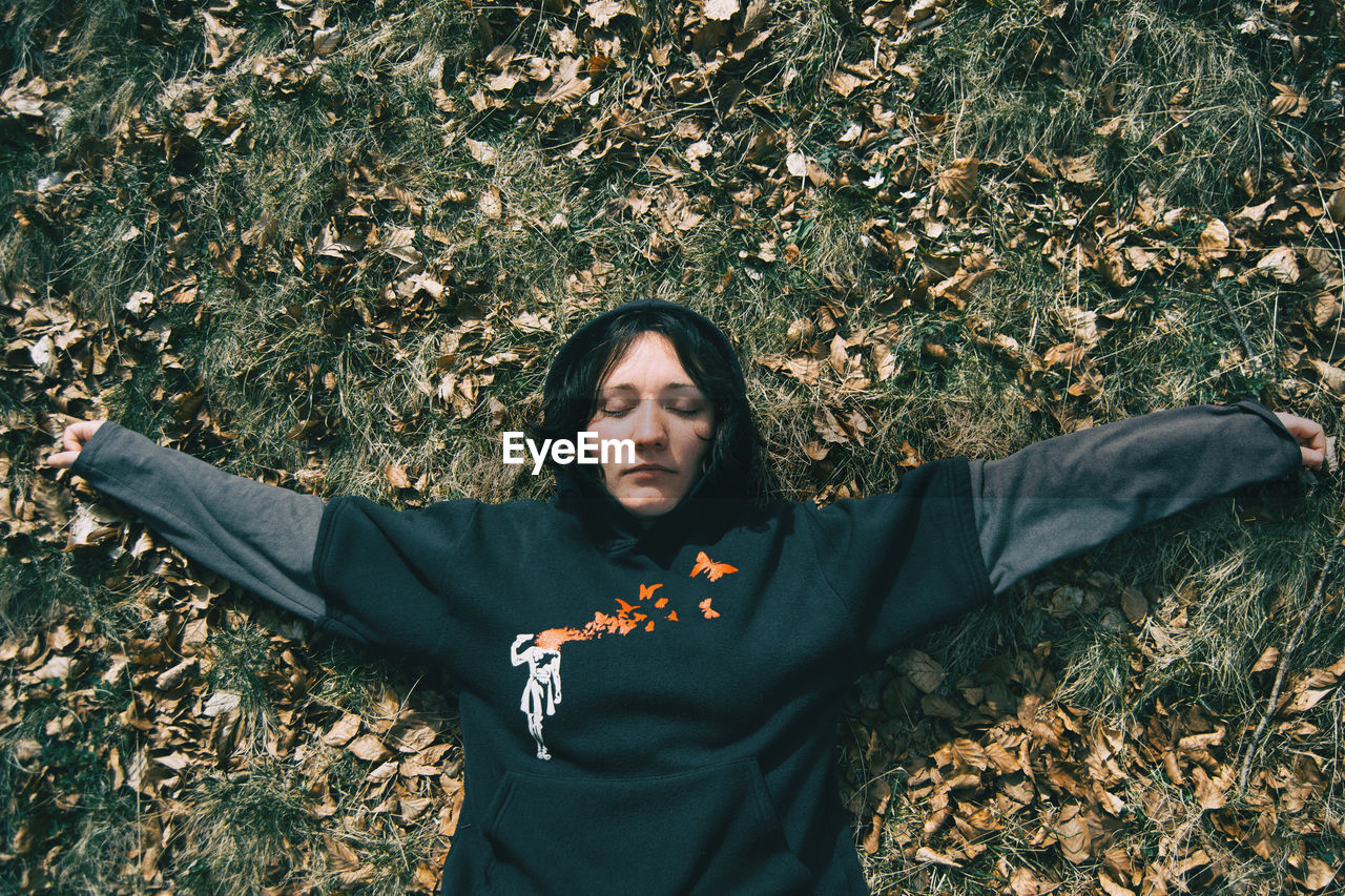 A girl with closed eyes and arms crossed resting on the ground in nature