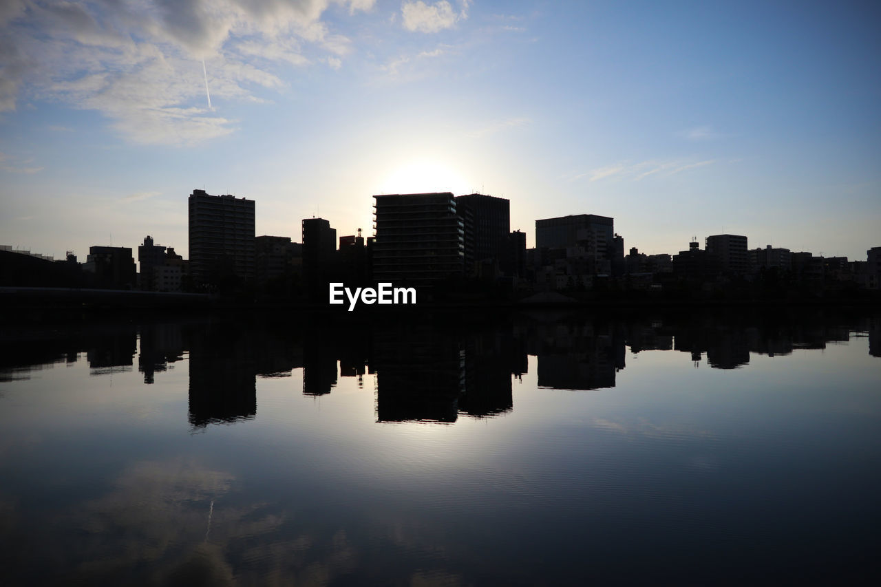 REFLECTION OF SILHOUETTE BUILDINGS IN LAKE DURING SUNSET