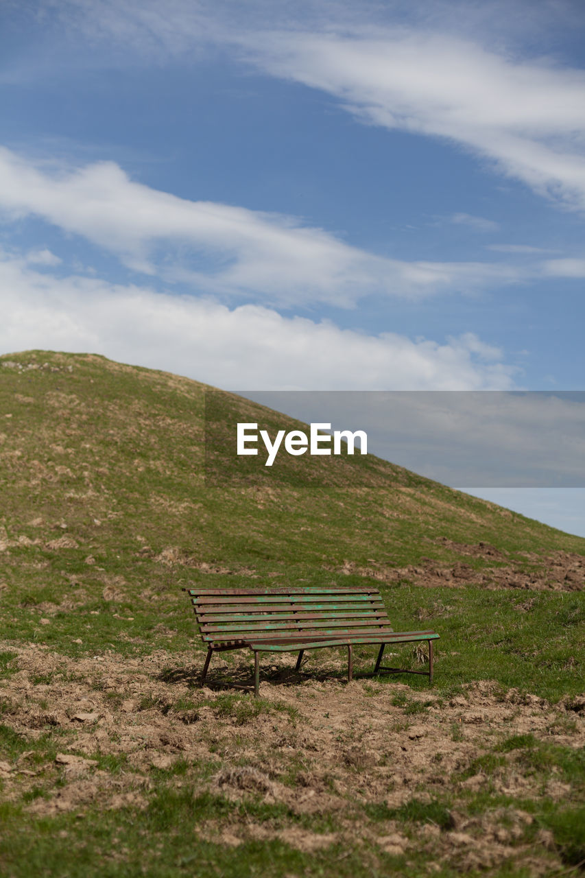 Empty bench on field against sky