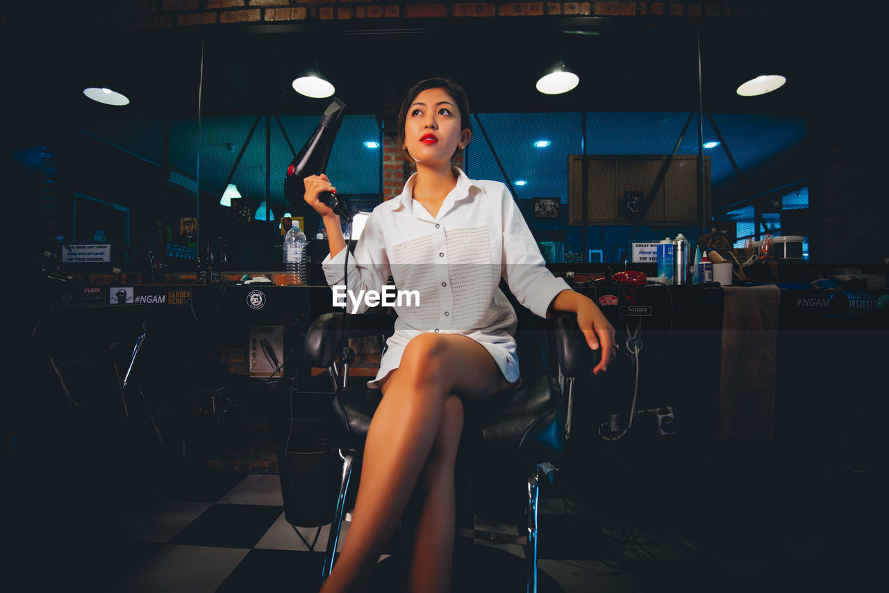 FULL LENGTH OF WOMAN SITTING ON SEAT IN ILLUMINATED ROOM