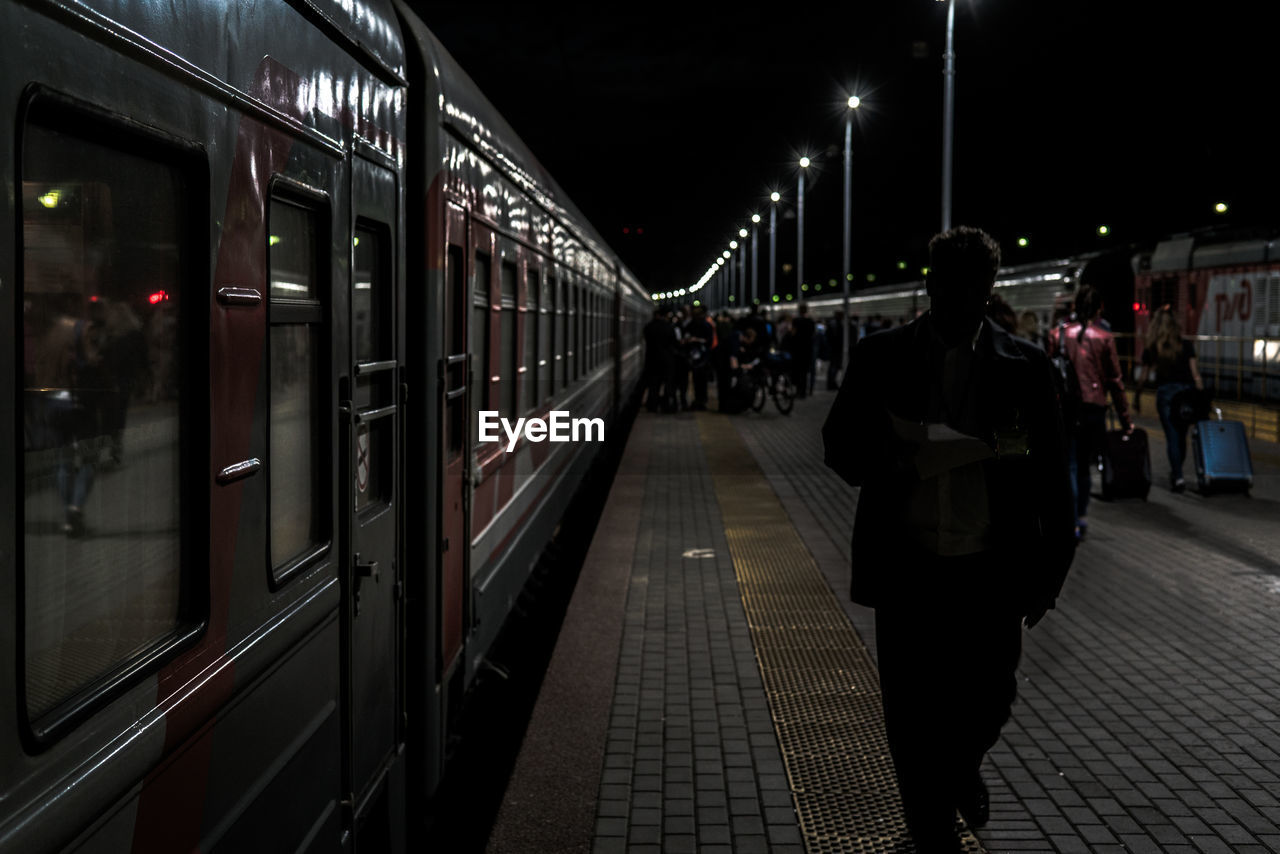 Rear view of man walking by train at railroad station during night