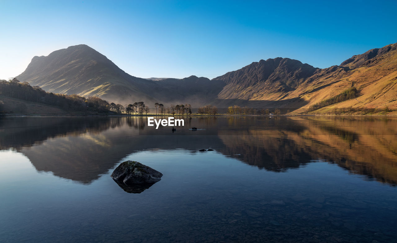 Scenic view of lake and mountains against clear blue sky