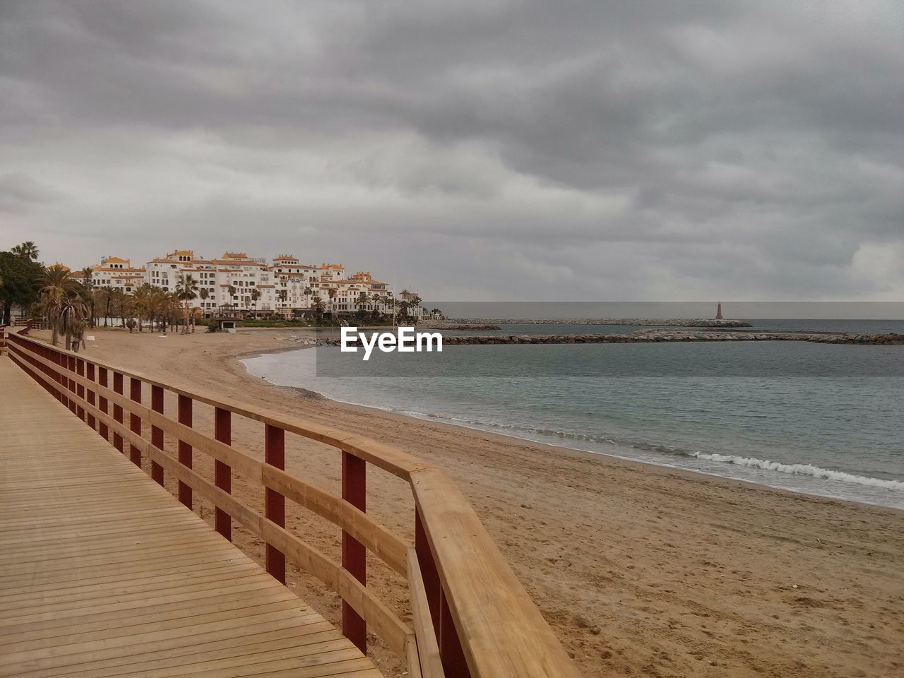 Boardwalk by beach against cloudy sky