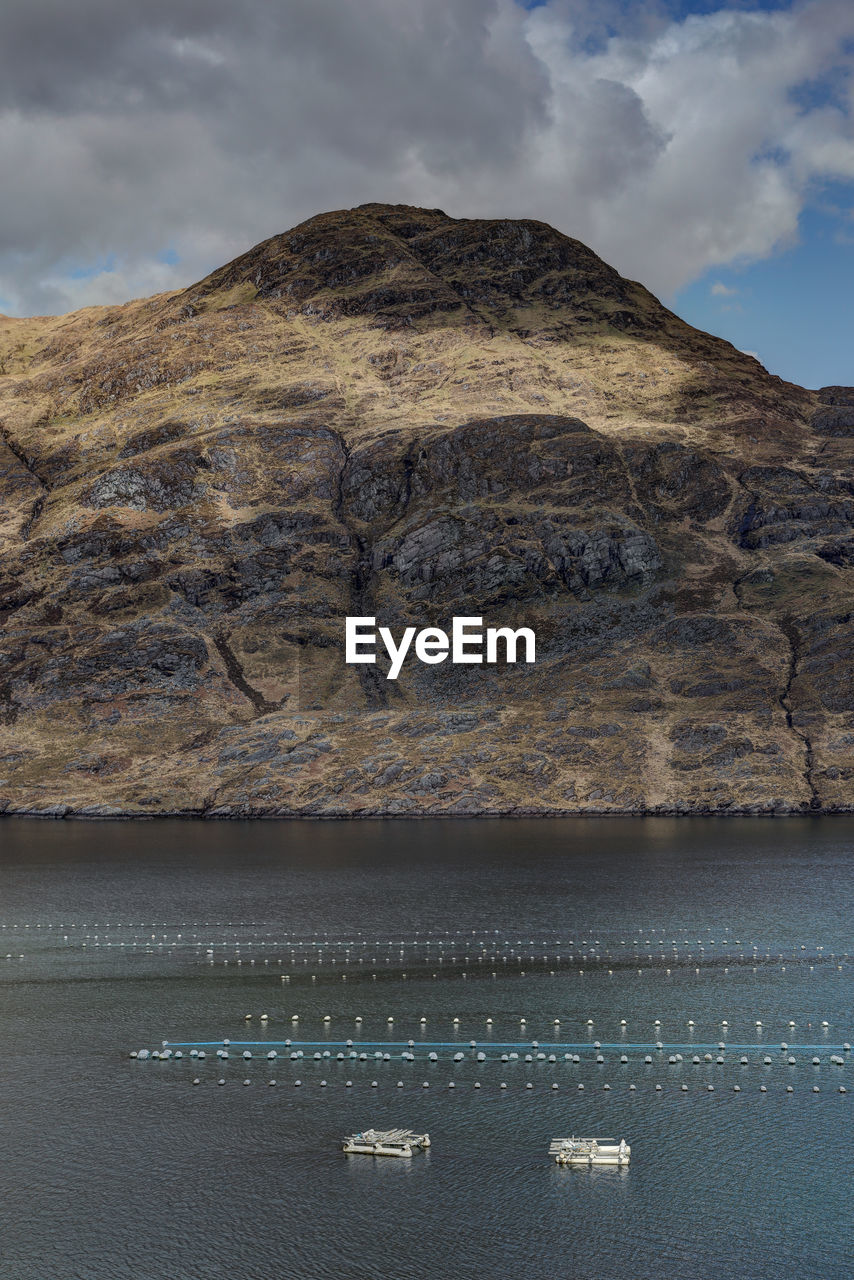 Mussel farming in lake amidst mountain against sky