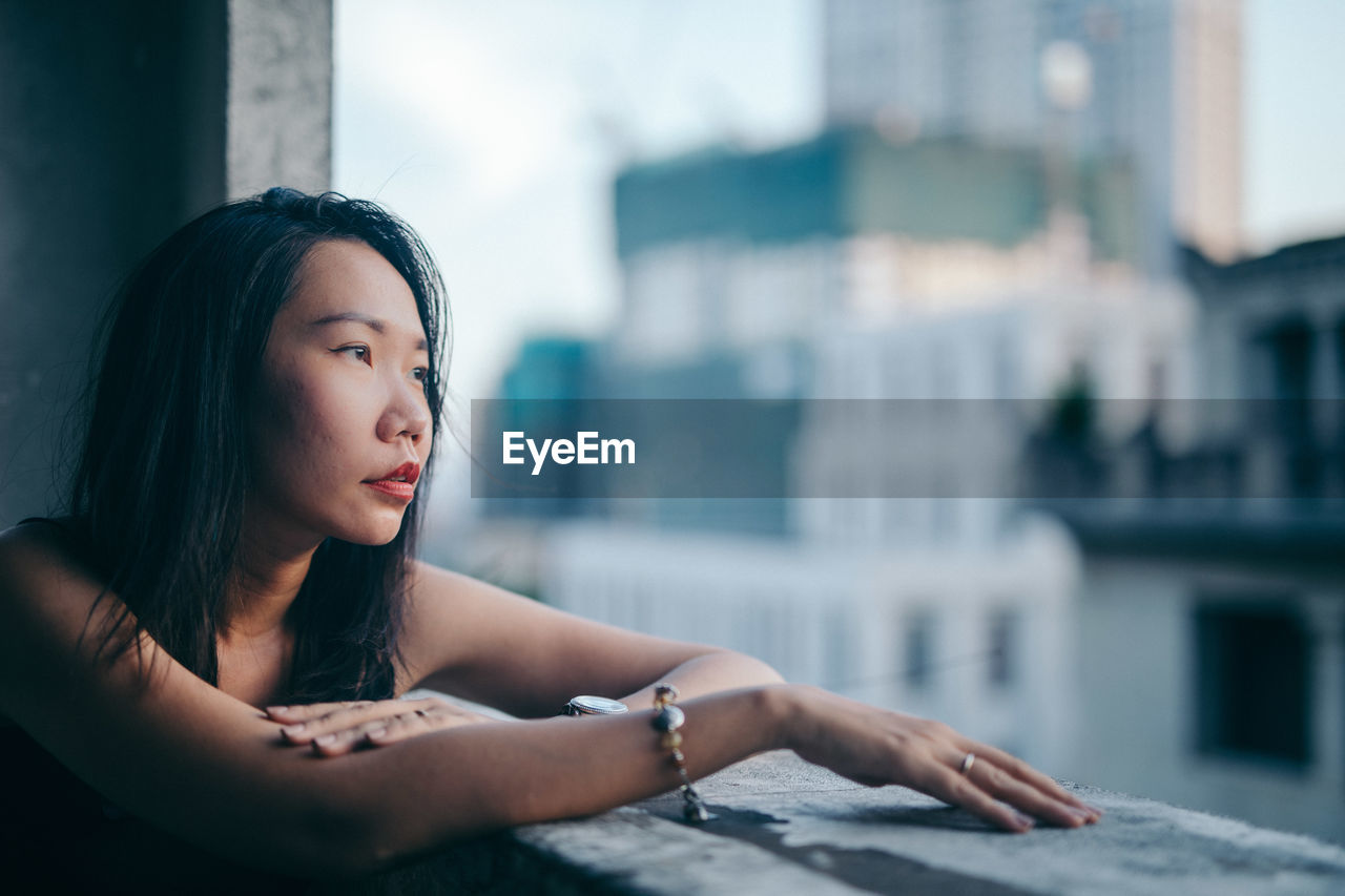 Thoughtful woman looking through window in city