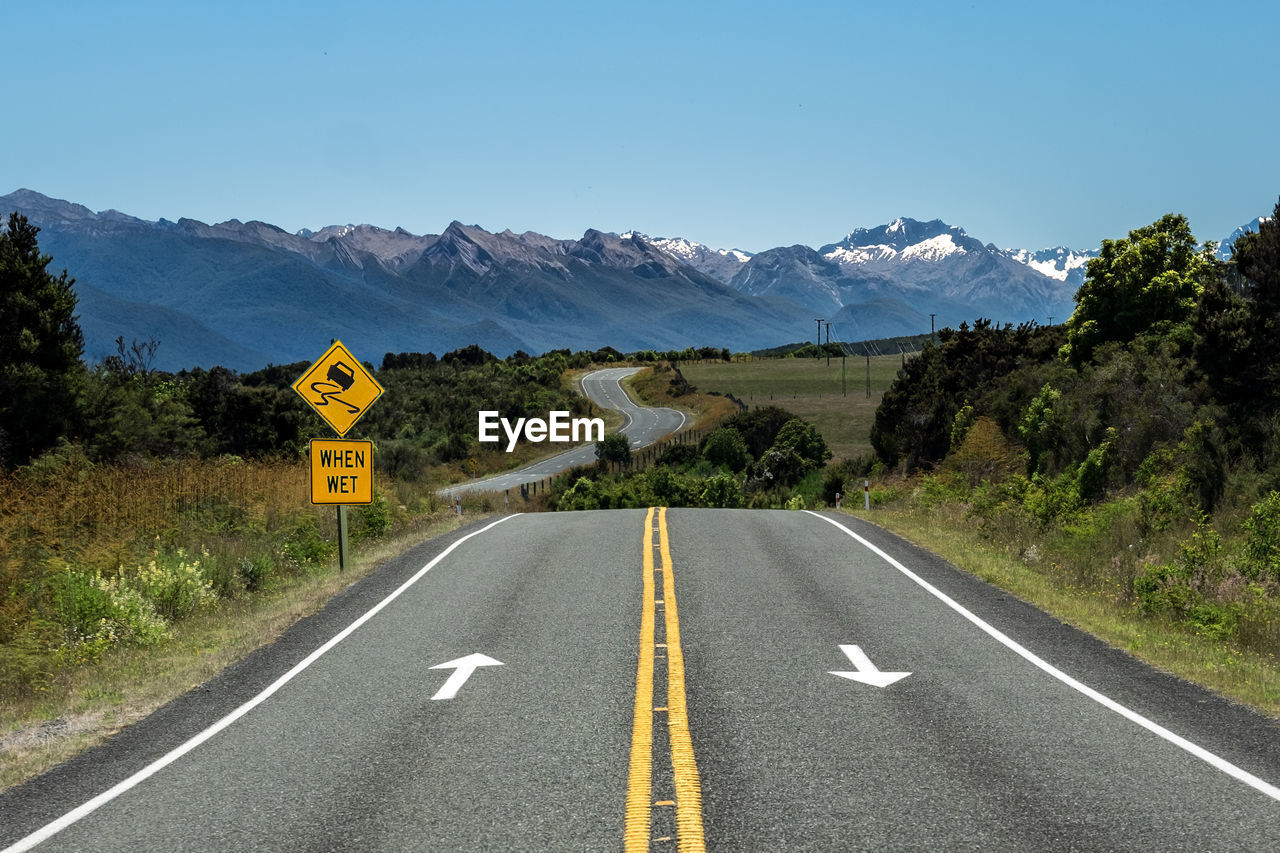 Road sign and zigzag road in new zealand against clear blue sky