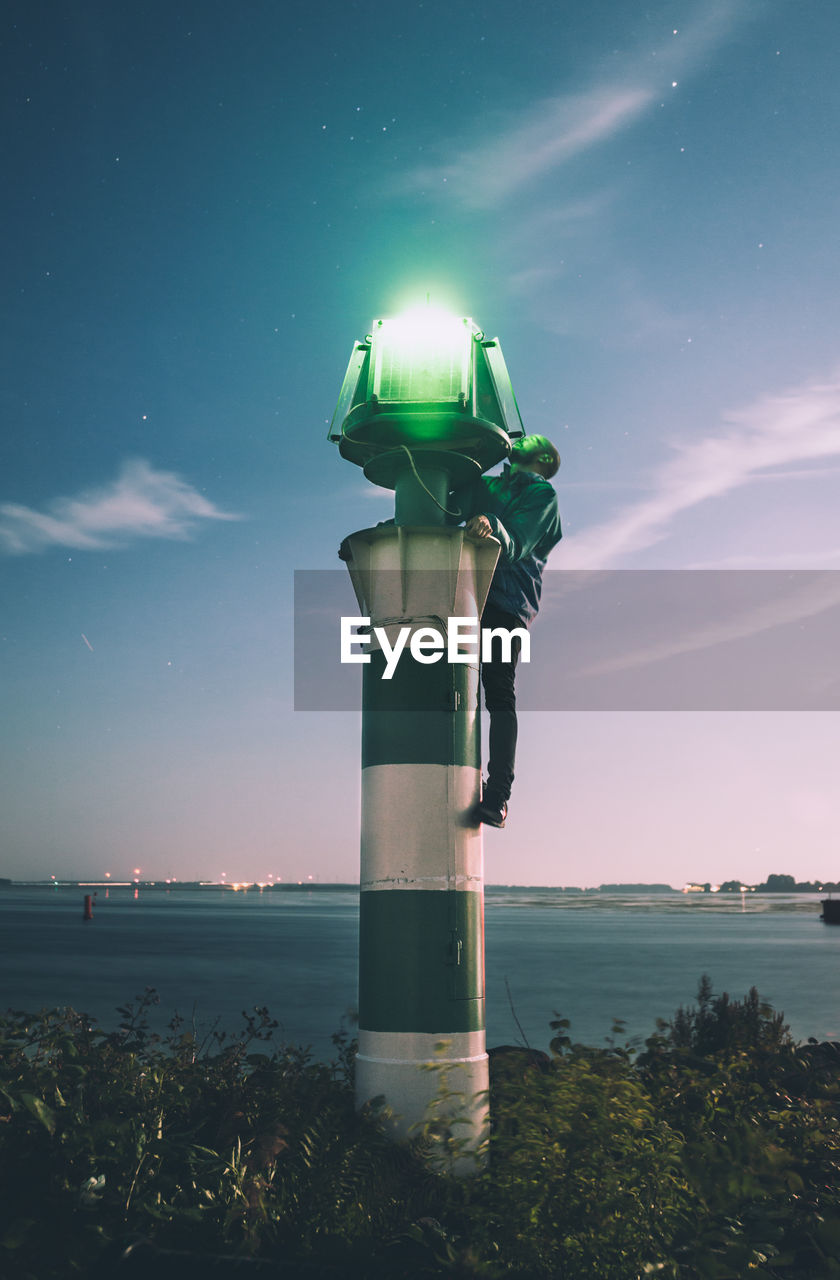 Man repairing lighthouse against sky at dusk