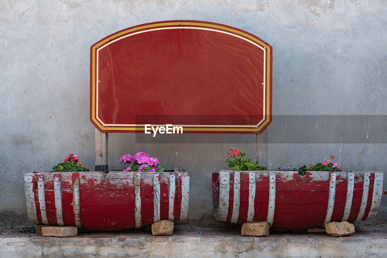 Red wooden signboard and frame in a garden and two small wooden vases with flowers.