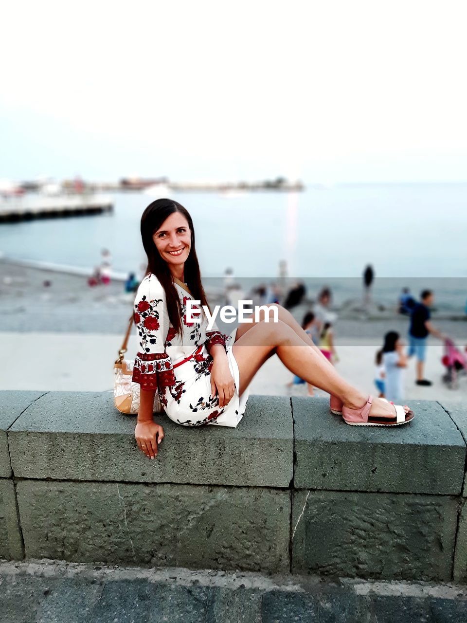 PORTRAIT OF YOUNG WOMAN SITTING AGAINST WALL