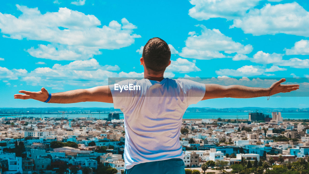 Rear view of man standing by cityscape against sky