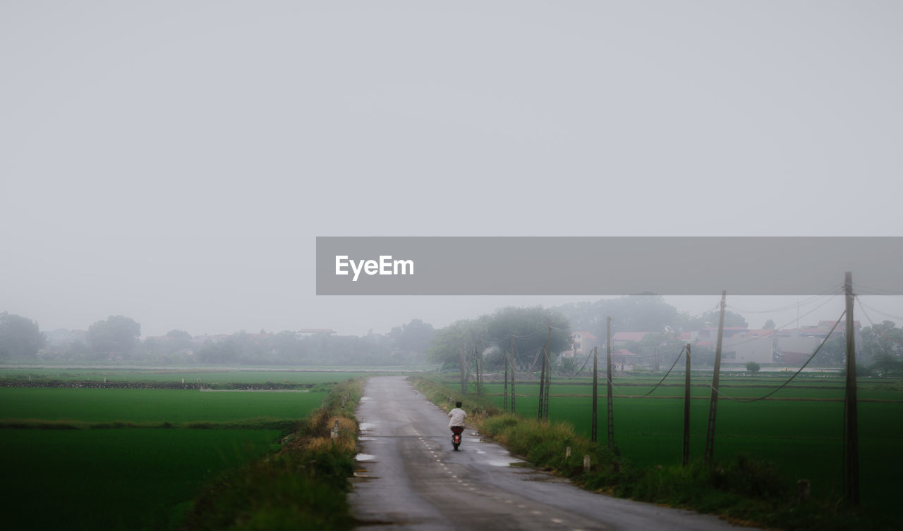 Man walking on road amidst field against sky