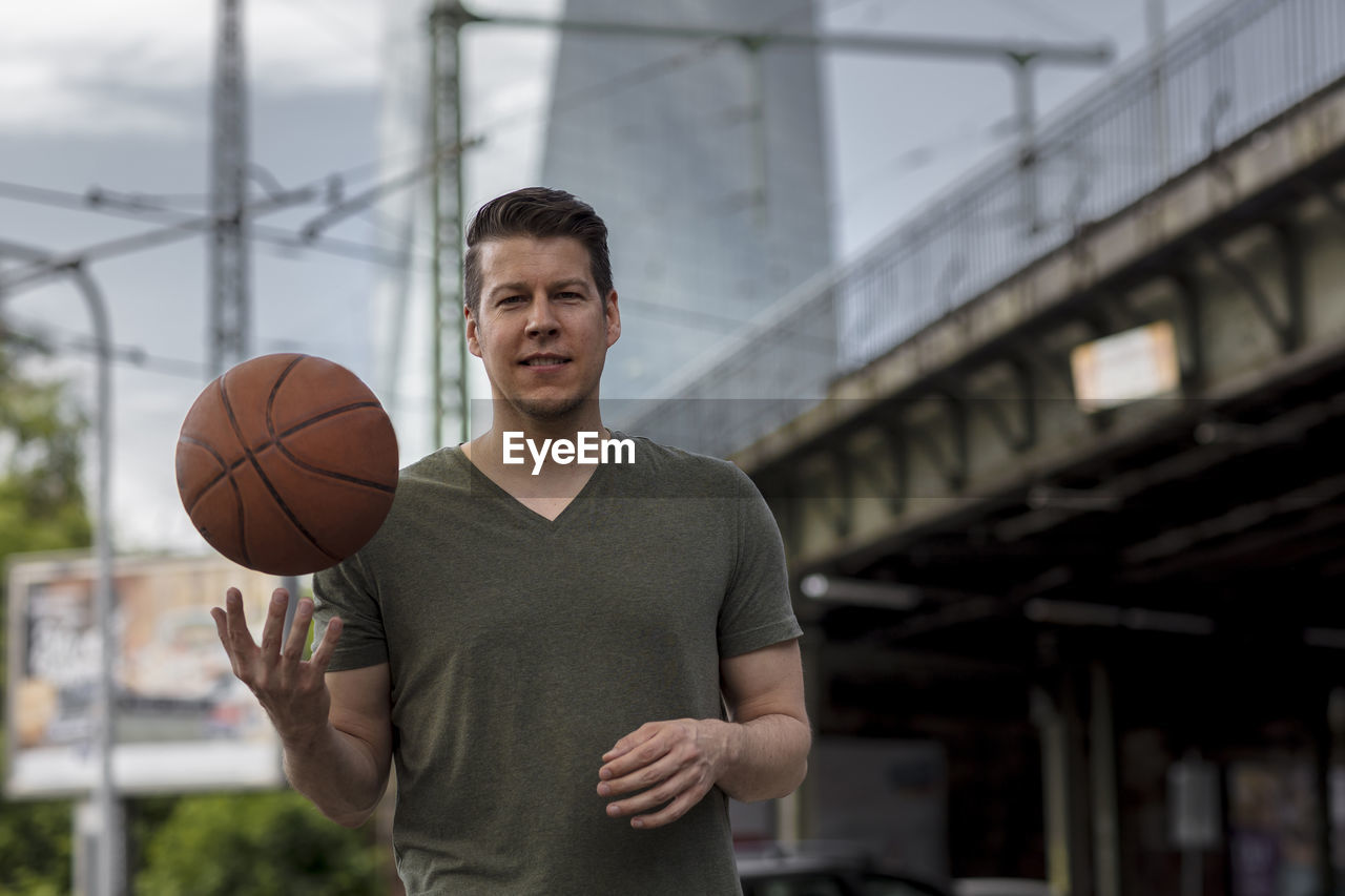 Portrait of young man with basketball standing outdoors