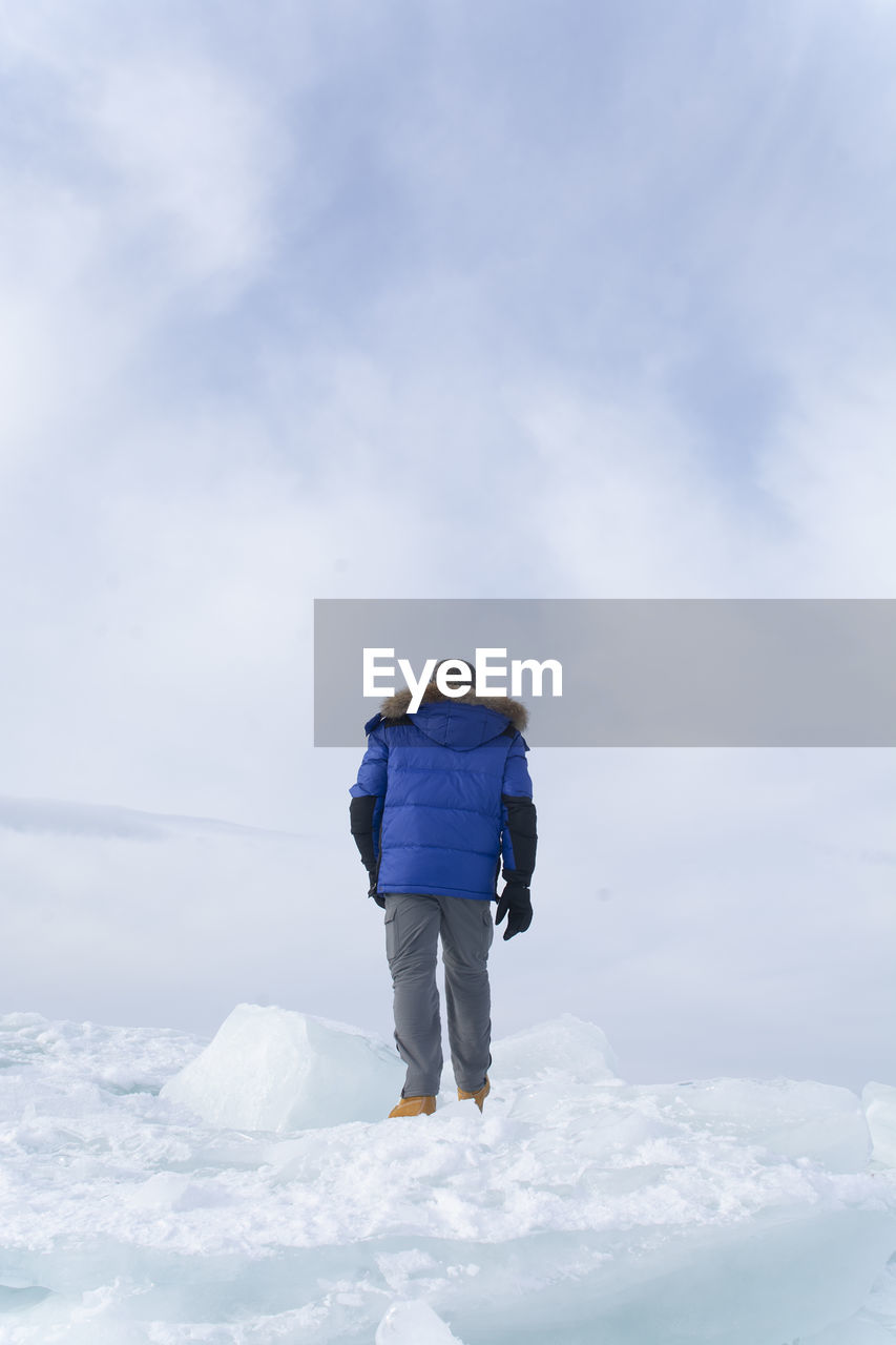 Rear view of man walking on snow against sky