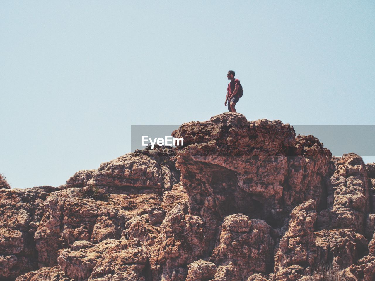 Low angle view of man standing on rock against clear sky