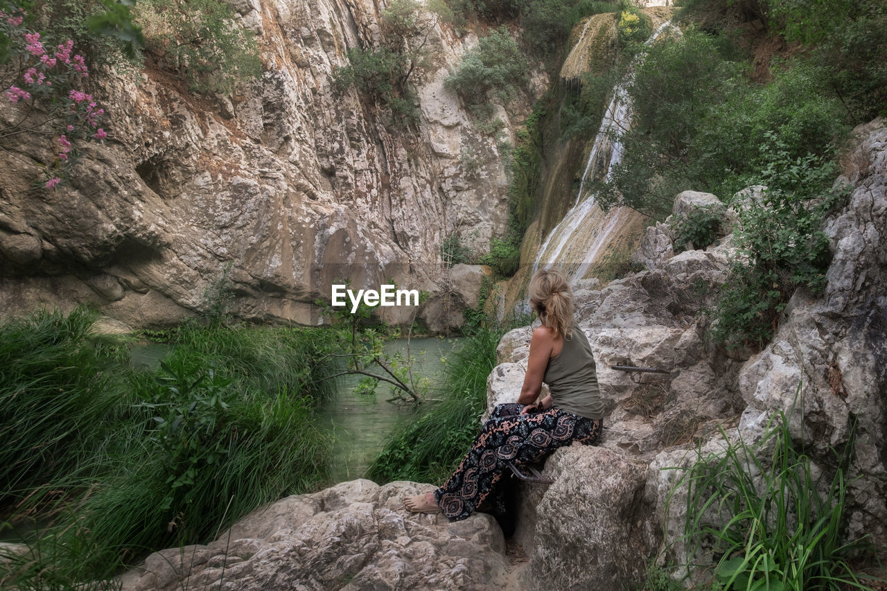 Woman sitting on rock next to a waterfall enjoying nature