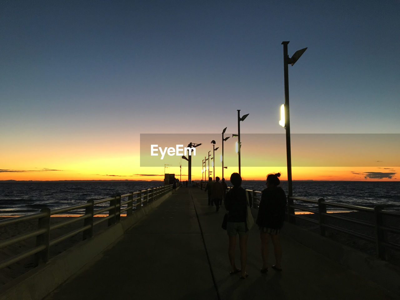 Silhouette people walking on pier towards sea against sky during sunset