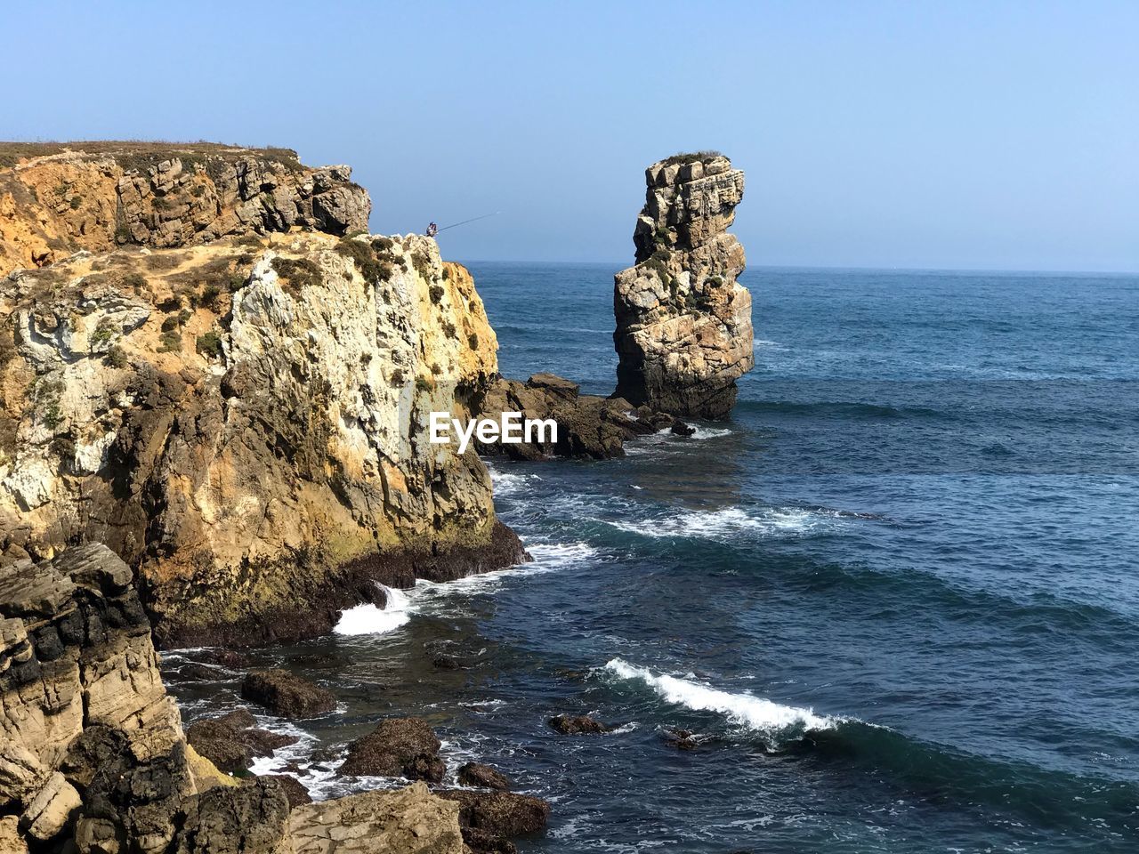 Scenic view of rocks in sea against clear blue sky