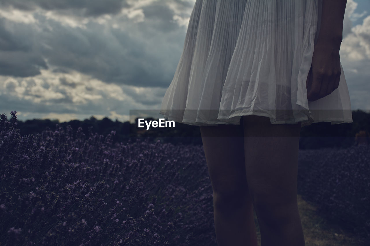Midsection of woman standing in field against cloudy sky