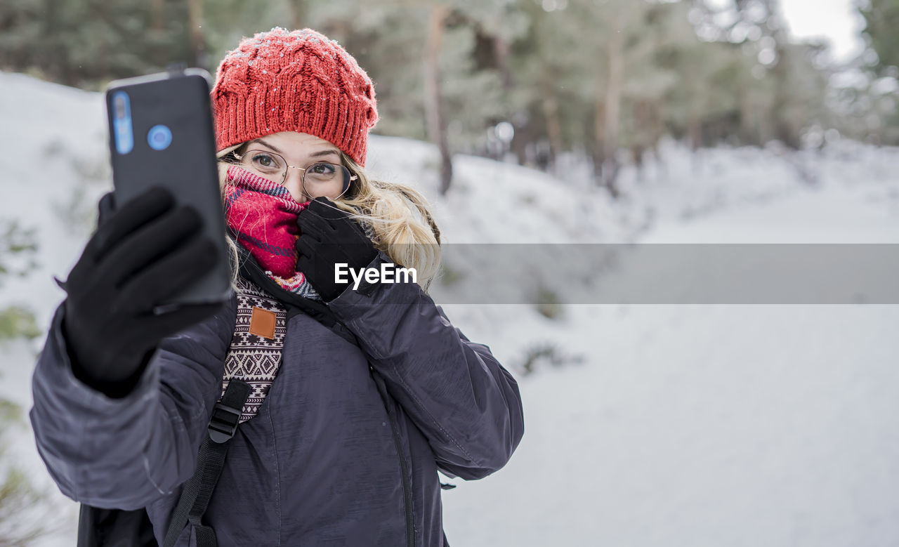 Cheerful young woman doing selfie while standing outdoors during winter